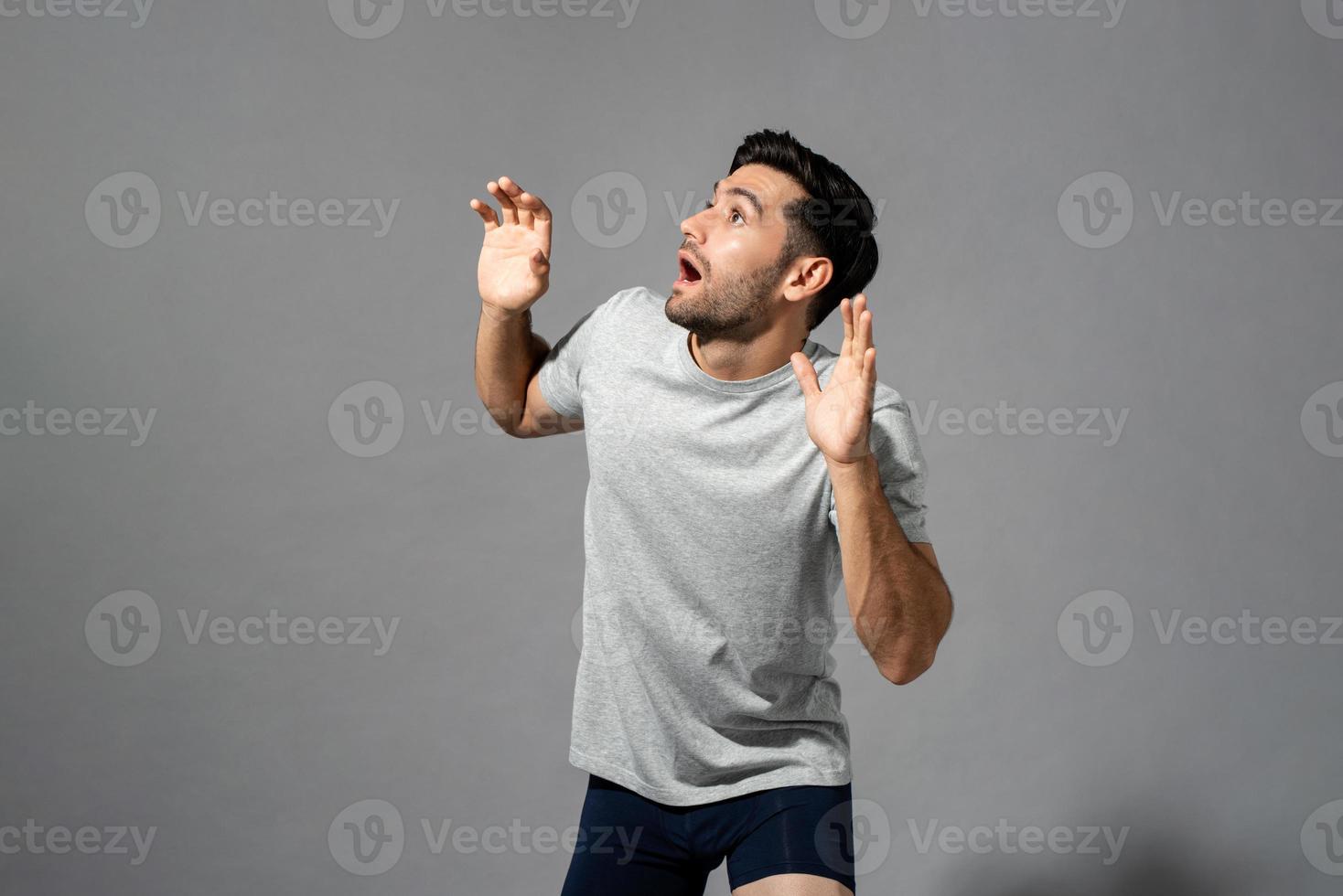 Überraschter schockierter junger kaukasischer Mann mit offener Handgeste, der zur Seite schaut und auf hellgrauem, isoliertem Studiohintergrund keucht foto