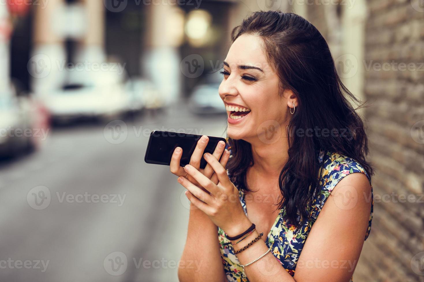 lächelnde junge Frau, die eine Sprachnotiz in ihrem Smartphone aufnimmt foto