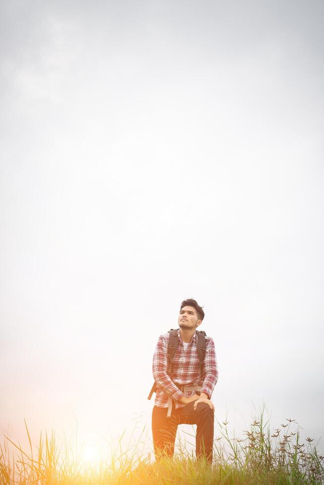 Porträt eines jungen Hipster-Mannes im Freien, der die Hände mit Rucksack auf der Schulter hebt, Abenteuertourismus. foto