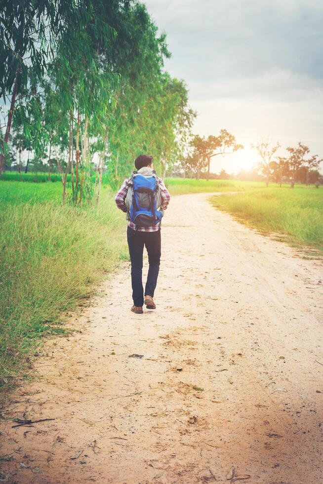 Rücken eines jungen Hipster-Mannes mit Rucksack auf der Schulter, der die Landschaft hinuntergeht. foto