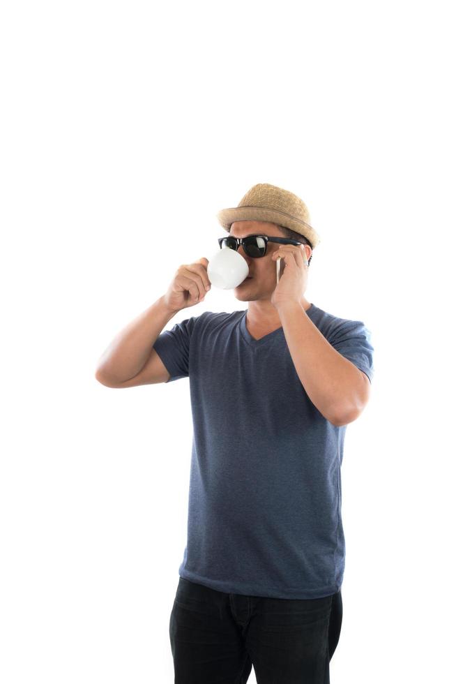 hübscher Hippie-Junger Mann im Hut und in der Sonnenbrille, die auf Handy über weißem Hintergrund steht und spricht. foto