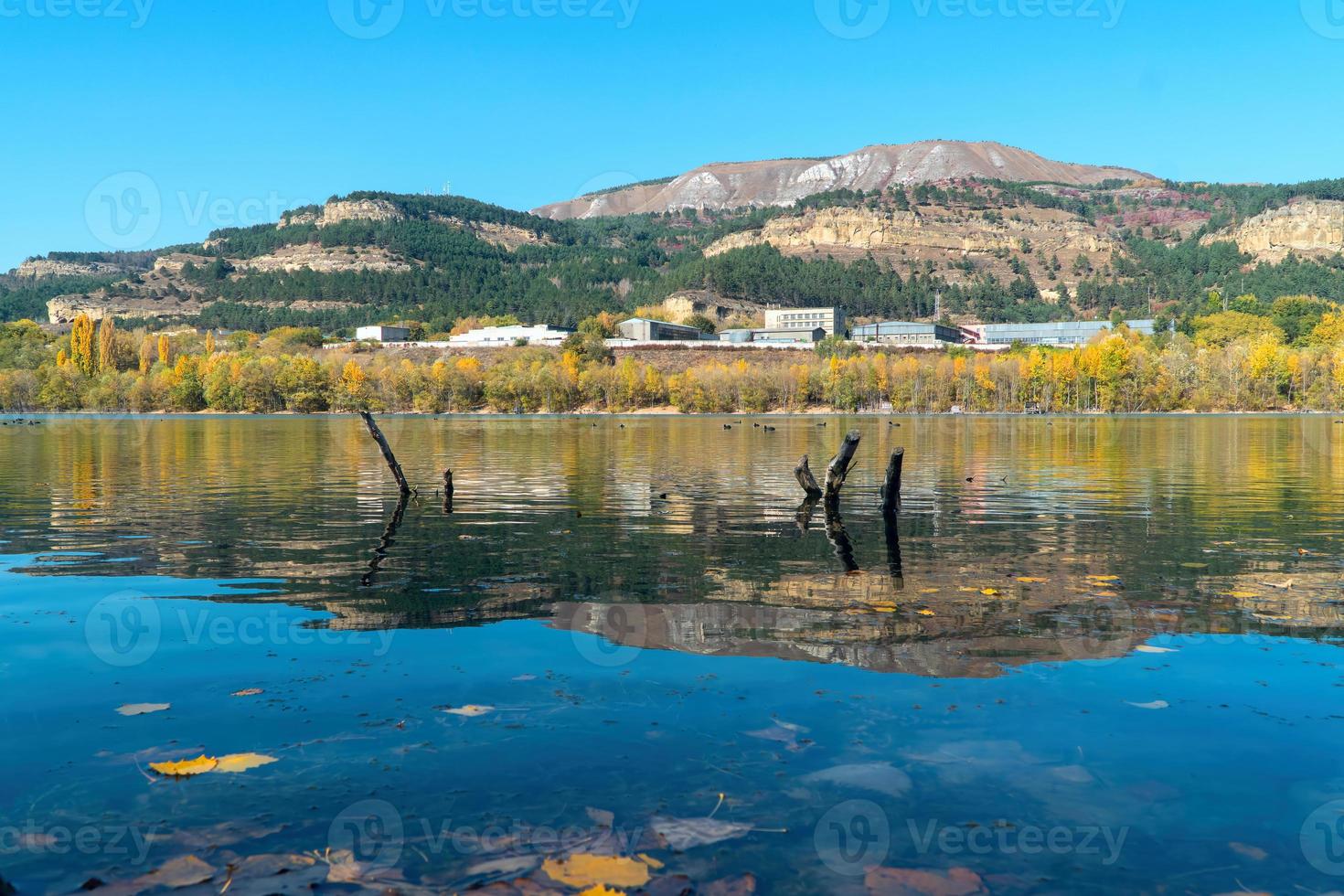 gelbe ahornblätter auf der blauen oberfläche des sees. Reflexion des Herbstwaldes und des Gebirgshintergrundes foto