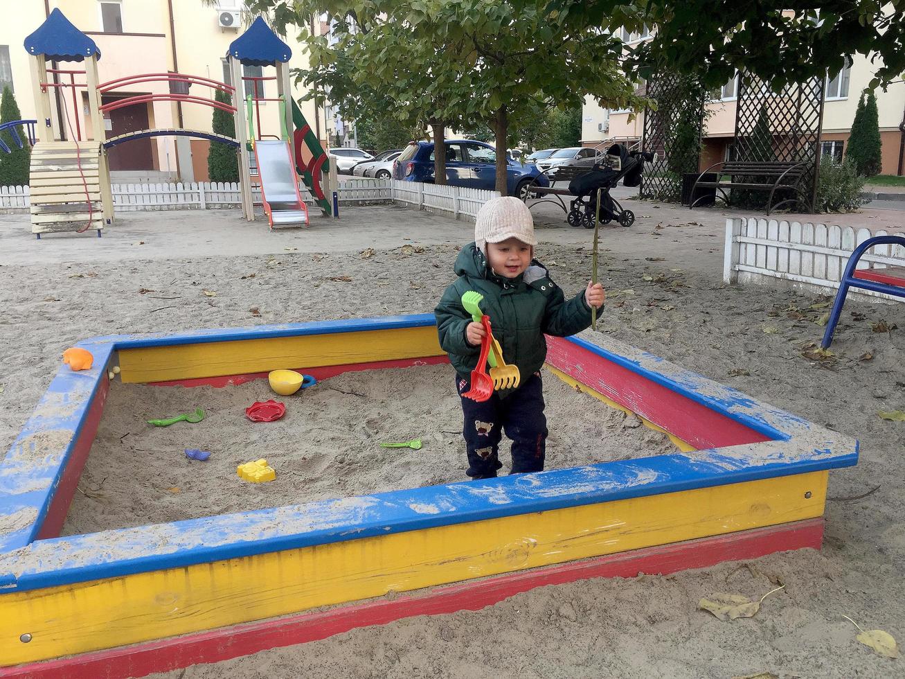 schönes Baby im Kindersandkasten posiert Fotograf in der Nähe von Sandkasten foto