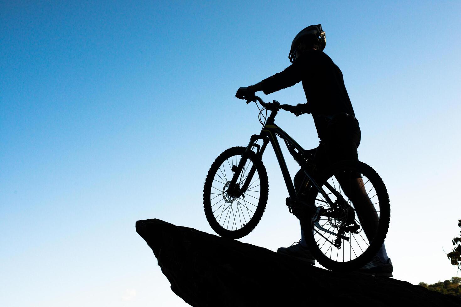 Silhouette des Athleten, der mit dem Fahrrad auf dem Felsen steht foto