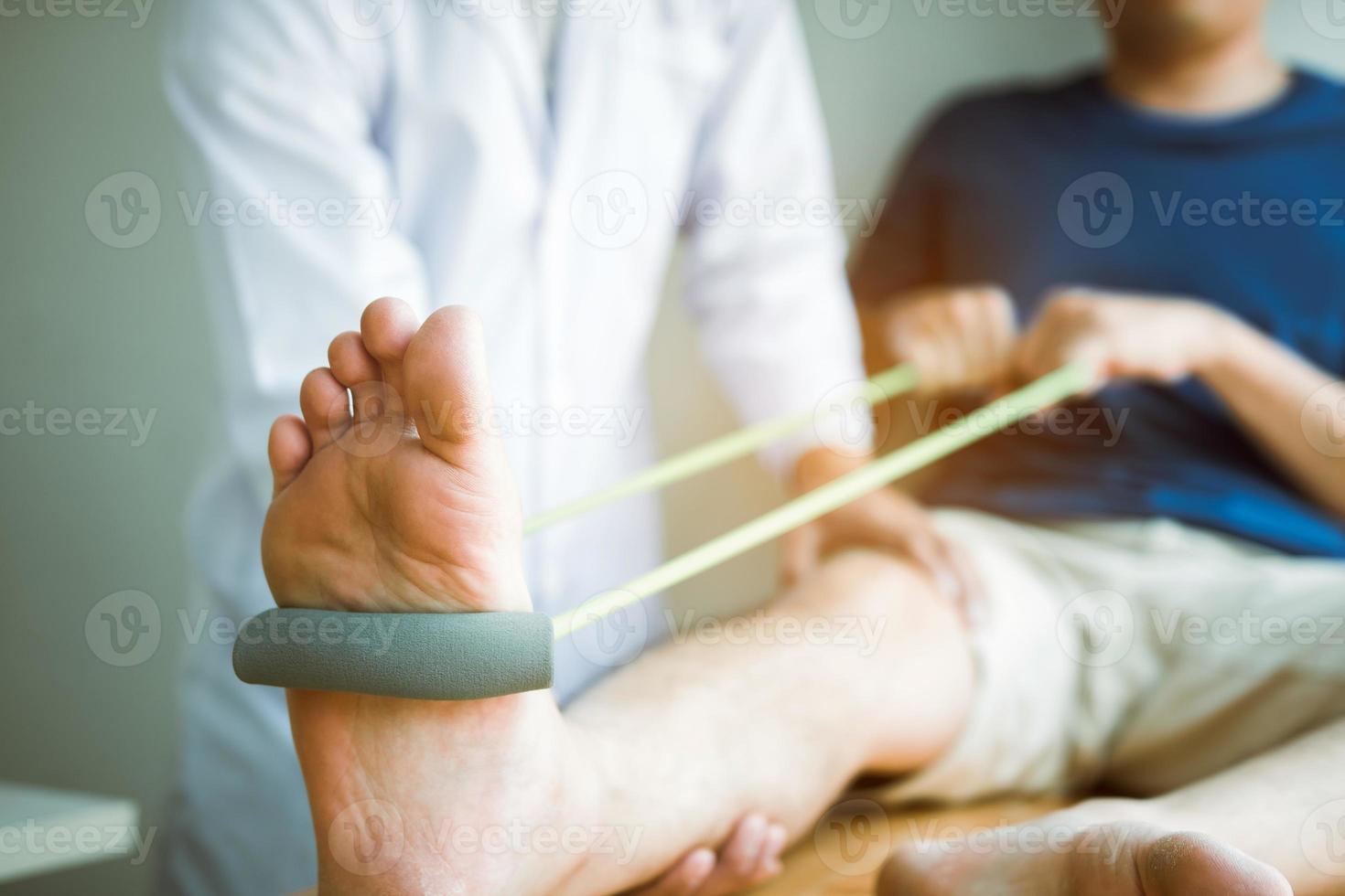 Der Patient verwendet ein Widerstandsband, das sein Bein mit einem Physiotherapeuten ausstreckt, und hilft im Klinikraum. foto