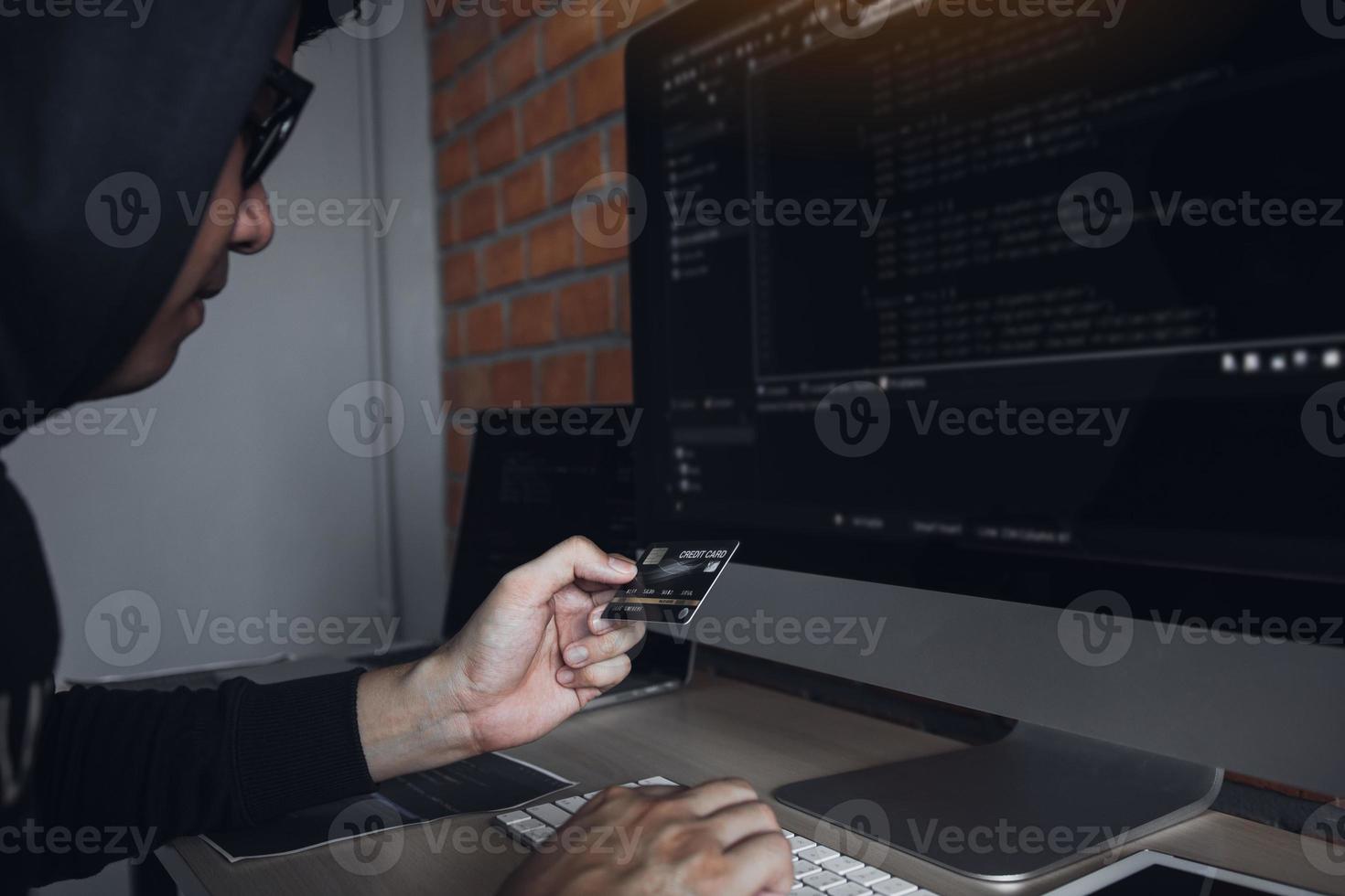 hacker in der haube, der mit computer arbeitet und kreditkarte mit zahlungs-hacking-konzept hält. foto