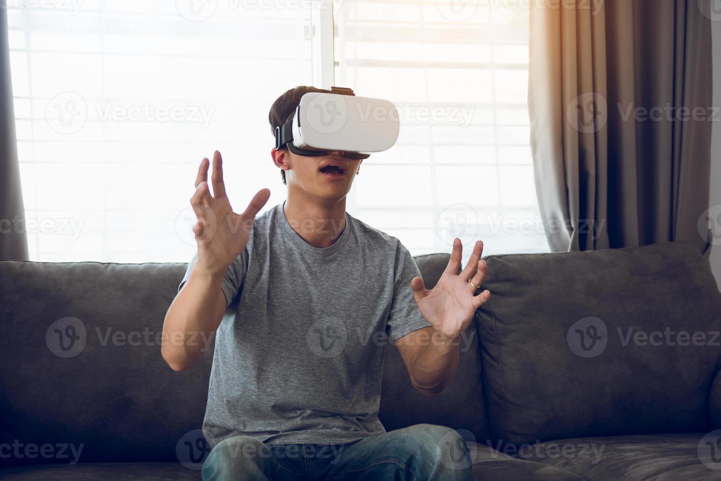 junger asiatischer mann, der im wohnzimmer eine virtual-reality-brille trägt, um die virtuelle realität zu bewundern. foto