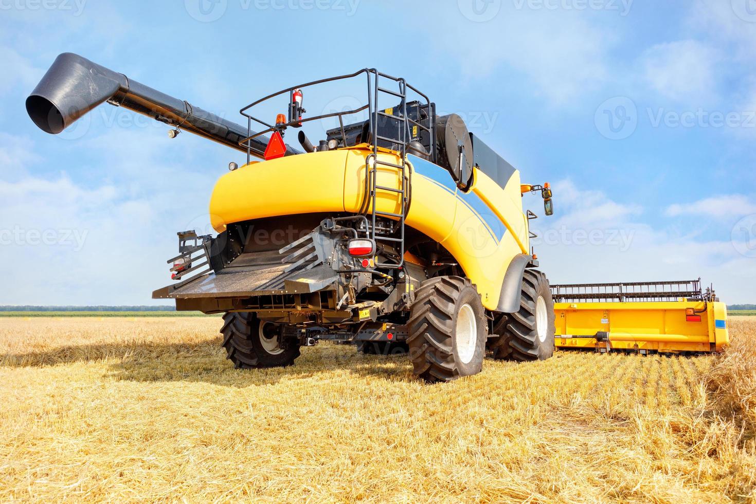 Ein großer gelber landwirtschaftlicher Mähdrescher, der an einem klaren Herbsttag vor dem Hintergrund eines Weizenfeldes Getreide erntet. foto