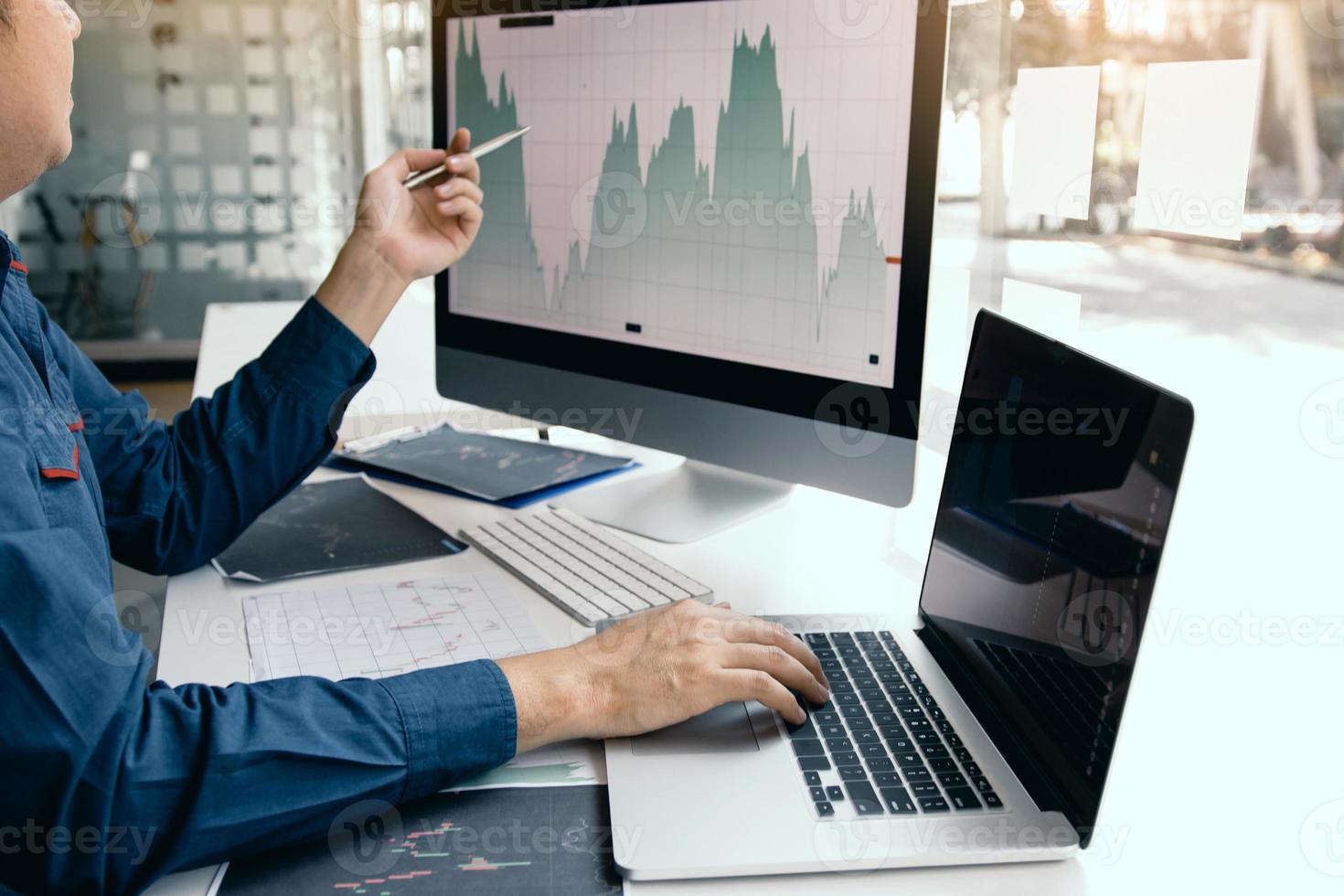 Investor-Mann, der das Diagramm des Aktienmarktes mit einem Stift analysiert, der auf den Computerbildschirm zeigt. foto