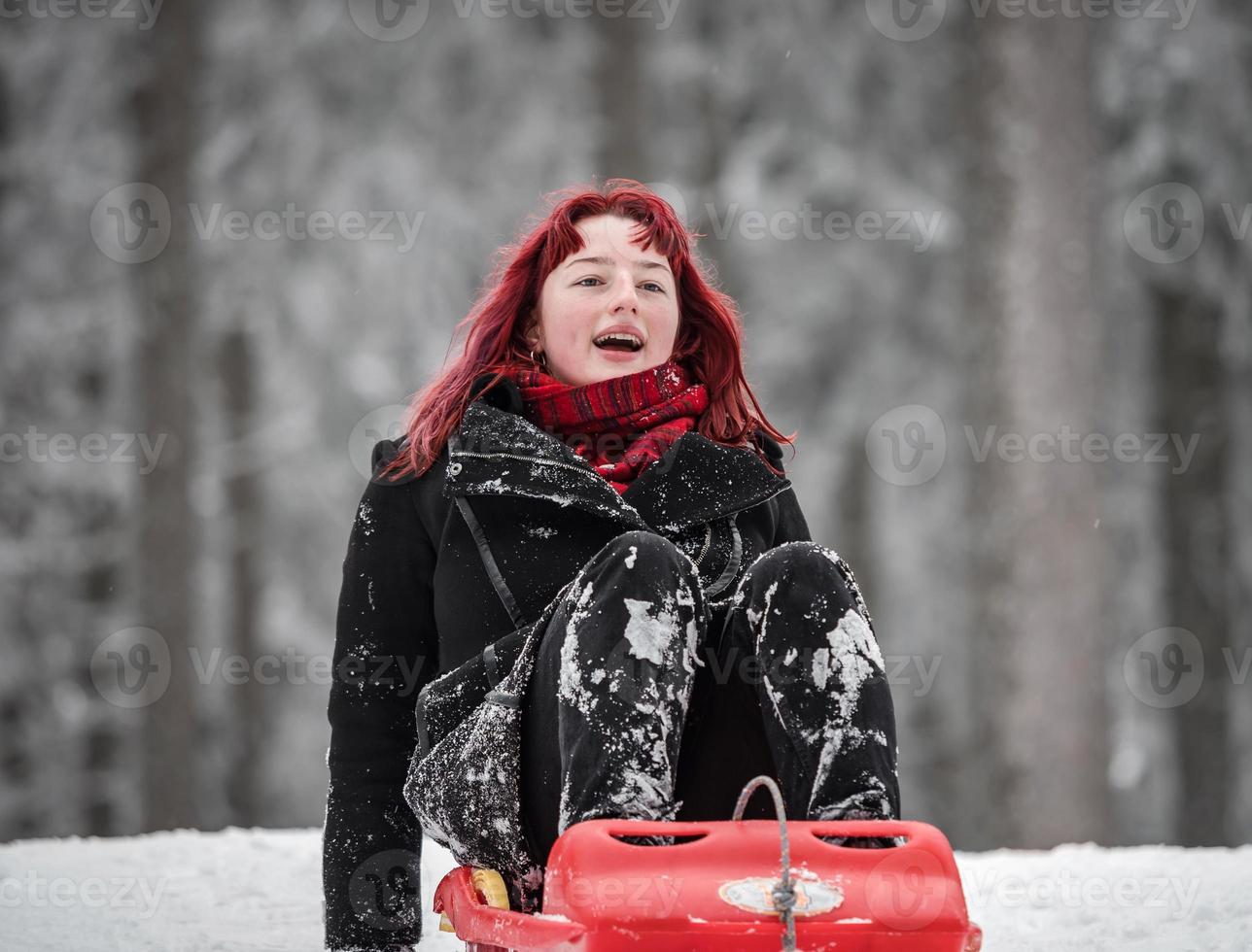 ein Mädchen mit roten Haarschlitten auf dem Winterschnee im Wald. foto