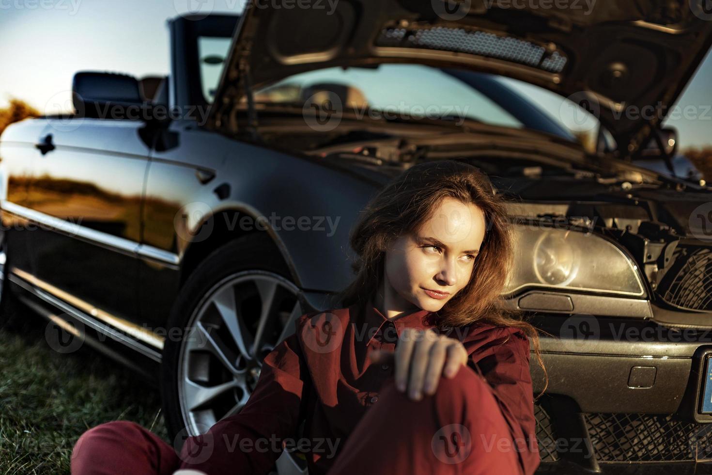 Ein schönes Mädchen in der Nähe eines Autos, das auf einem Feld kaputt ist, ein Retro-Cabriolet foto