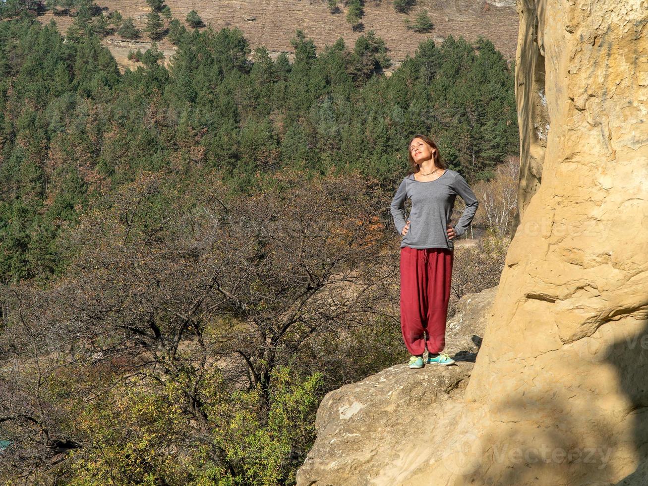 Frau mit Blick auf die Sonne auf einem Berg, gekleidet in indische Hosen, Porträt an einem Herbsttag foto