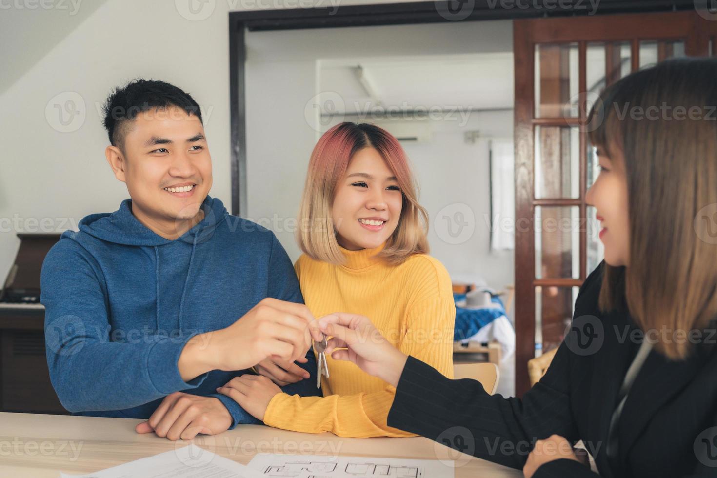 glückliches junges asiatisches Paar und Makleragent. fröhlicher junger Mann, der einige Dokumente unterschreibt und Händeschütteln mit Makler beim Sitzen am Schreibtisch. Unterzeichnung eines Vertrags über guten Zustand. foto