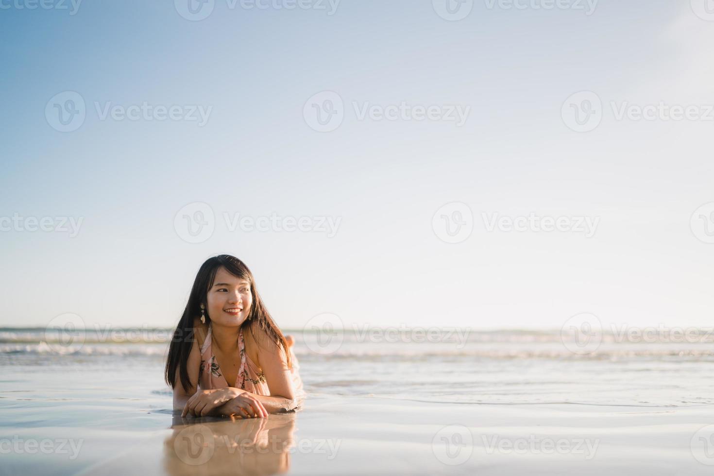 junge asiatische frau, die sich am strand glücklich fühlt, schöne weibliche glückliche entspannen lächelnden spaß am strand in der nähe des meeres bei sonnenuntergang am abend. Lifestyle-Frauen reisen am Strandkonzept. foto