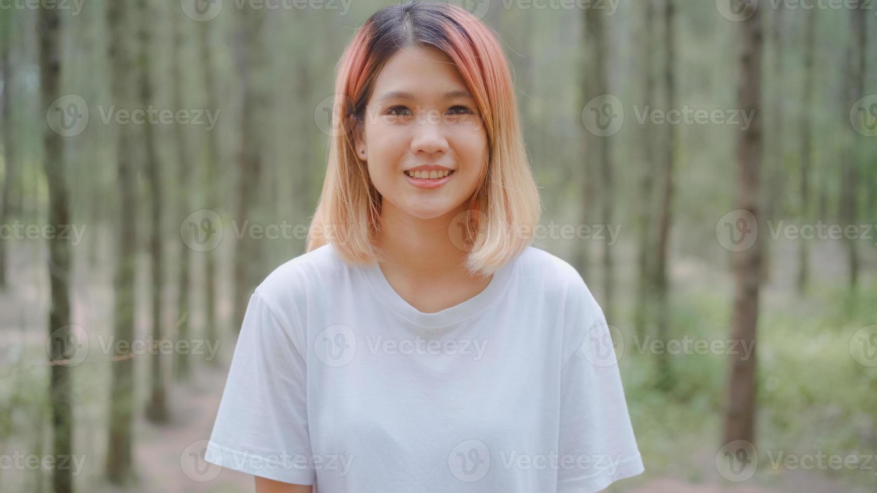 gesunde schöne junge asiatische Läuferfrau, die das glückliche Lächeln und das Schauen zur Kamera nach dem Laufen auf Waldweg fühlt. Lifestyle Fit und aktive Frauen trainieren im Waldkonzept. foto