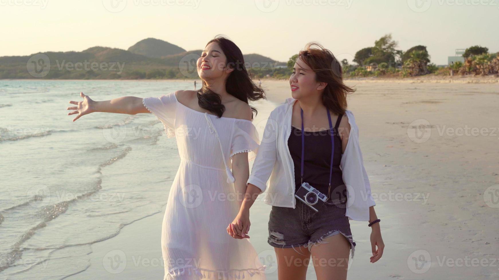 junges asiatisches lesbisches Paar, das am Strand spazieren geht. schöne freundinnen glücklich entspannen am strand in der nähe des meeres spazieren, wenn sonnenuntergang am abend. Lebensstil lesbisches Paar reist am Strandkonzept. foto