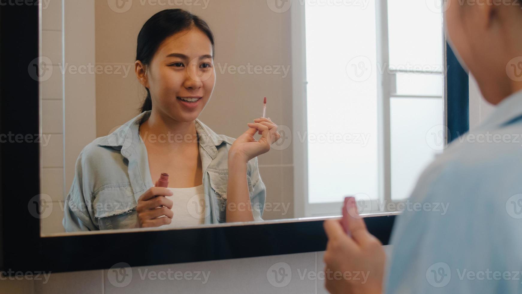 schöne asiatische frau, die lippenstift verwendet, schminken sich im vorderen spiegel, glückliche chinesische frau, die schönheitskosmetik verwendet, um sich zu verbessern, bereit, zu hause im badezimmer zu arbeiten. Lifestyle-Frauen entspannen sich zu Hause foto