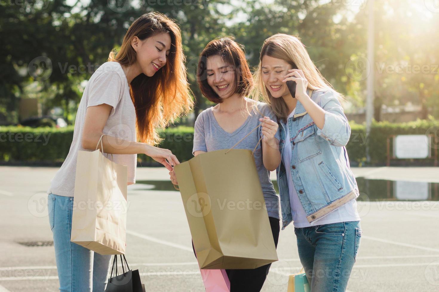 Gruppe junger asiatischer Frauen, die mit Einkaufstüten in den Händen auf einem Markt im Freien einkaufen. junge frauen zeigen bei warmem sonnenlicht, was sie in der einkaufstasche haben. gruppen-outdoor-shopping-konzept. foto