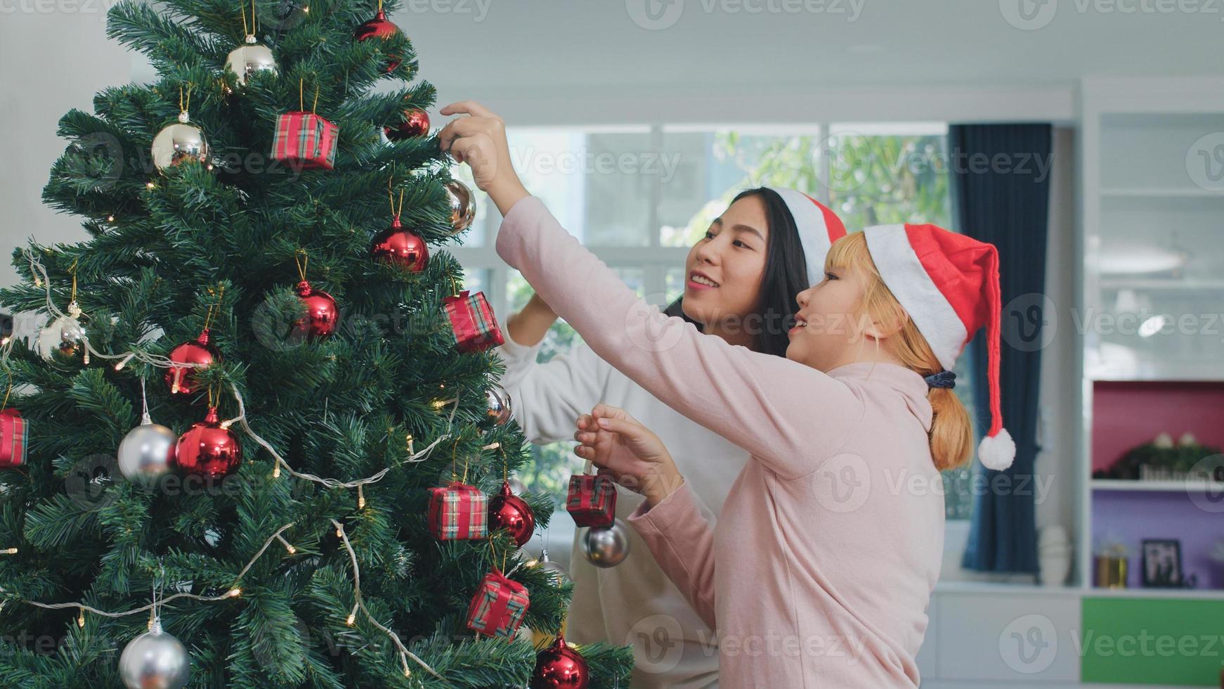 asiatische Freundinnen schmücken den Weihnachtsbaum beim Weihnachtsfest. Weibliche Teenager glücklich lächelnd feiern Weihnachten Winterferien zusammen im Wohnzimmer zu Hause. foto