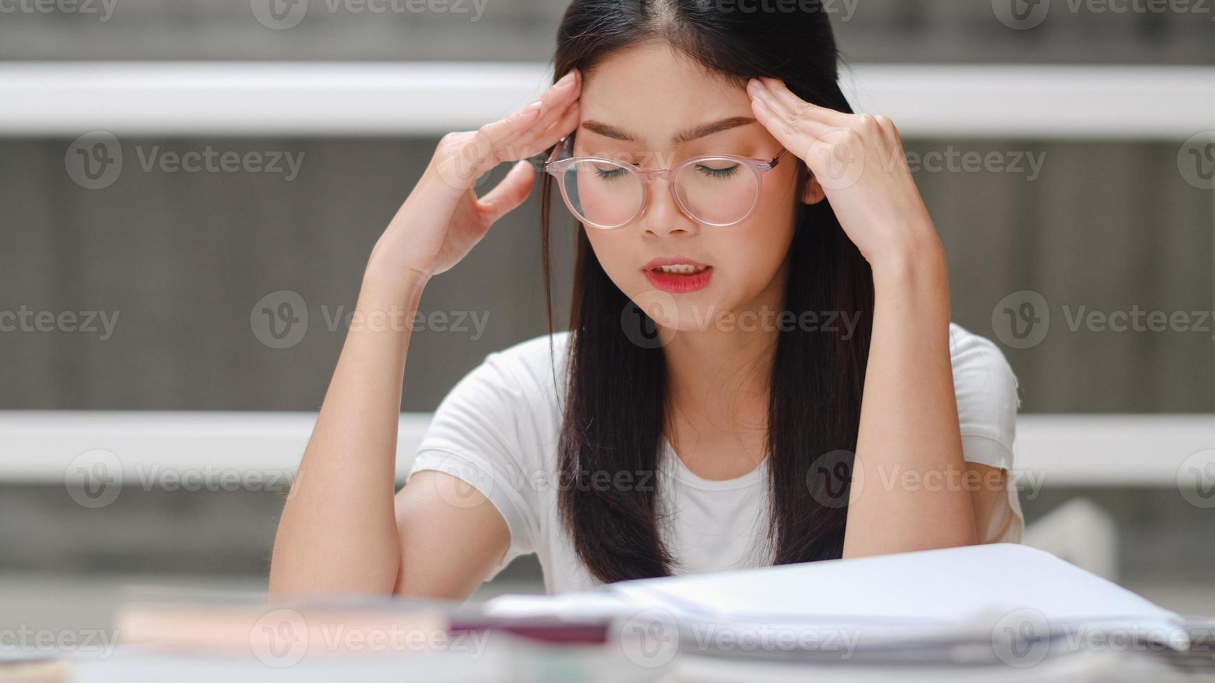 asiatische studentinnen lesen bücher in der bibliothek der universität. junge Studentin stressmüde haben Probleme, während sie hart lernen, um Wissen auf dem Hörpult am College-Campus-Konzept zu erlangen. foto