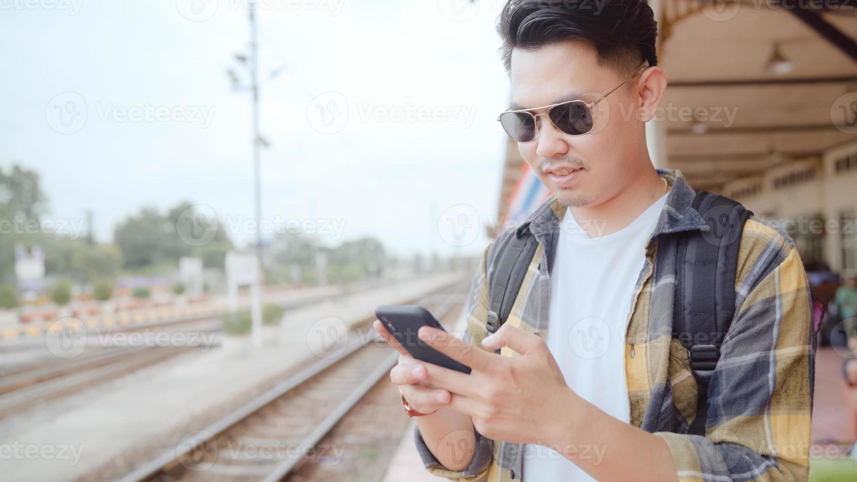 asiatischer rucksackmann am bahnhof, junger männlicher touristenrucksacktourist, der auf seiner reise in thailand handy-blick und richtungskarten verwendet. Lebensstile Männer entspannen und reisen Konzept. foto