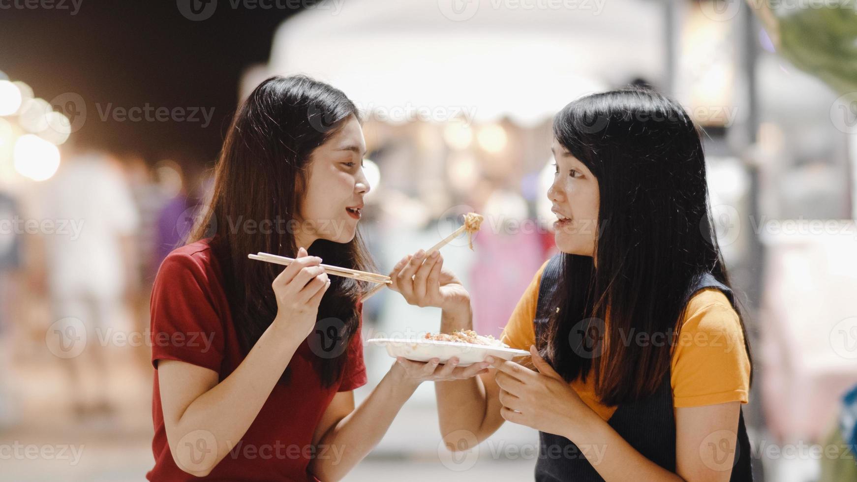 asiatische junge freundinnen reisen in bangkok, thailand, schöne weibliche fühlen sich glücklich beim gehen und essen pad thai an der khao san road. frauen reisen essen straßenessen im thailand-konzept. foto