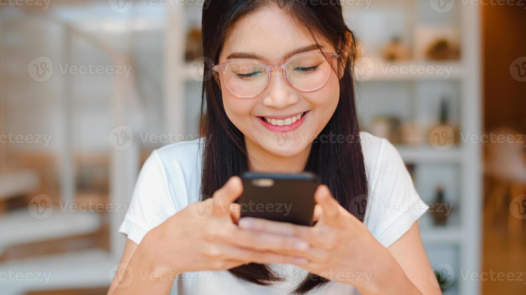 freiberufliche asiatische frauen, die im büro ein handy benutzen. junges japanisches asiatisches mädchen, das smartphone verwendet, das soziale medien im internet auf dem tisch am arbeitsplatzkonzept überprüft. foto