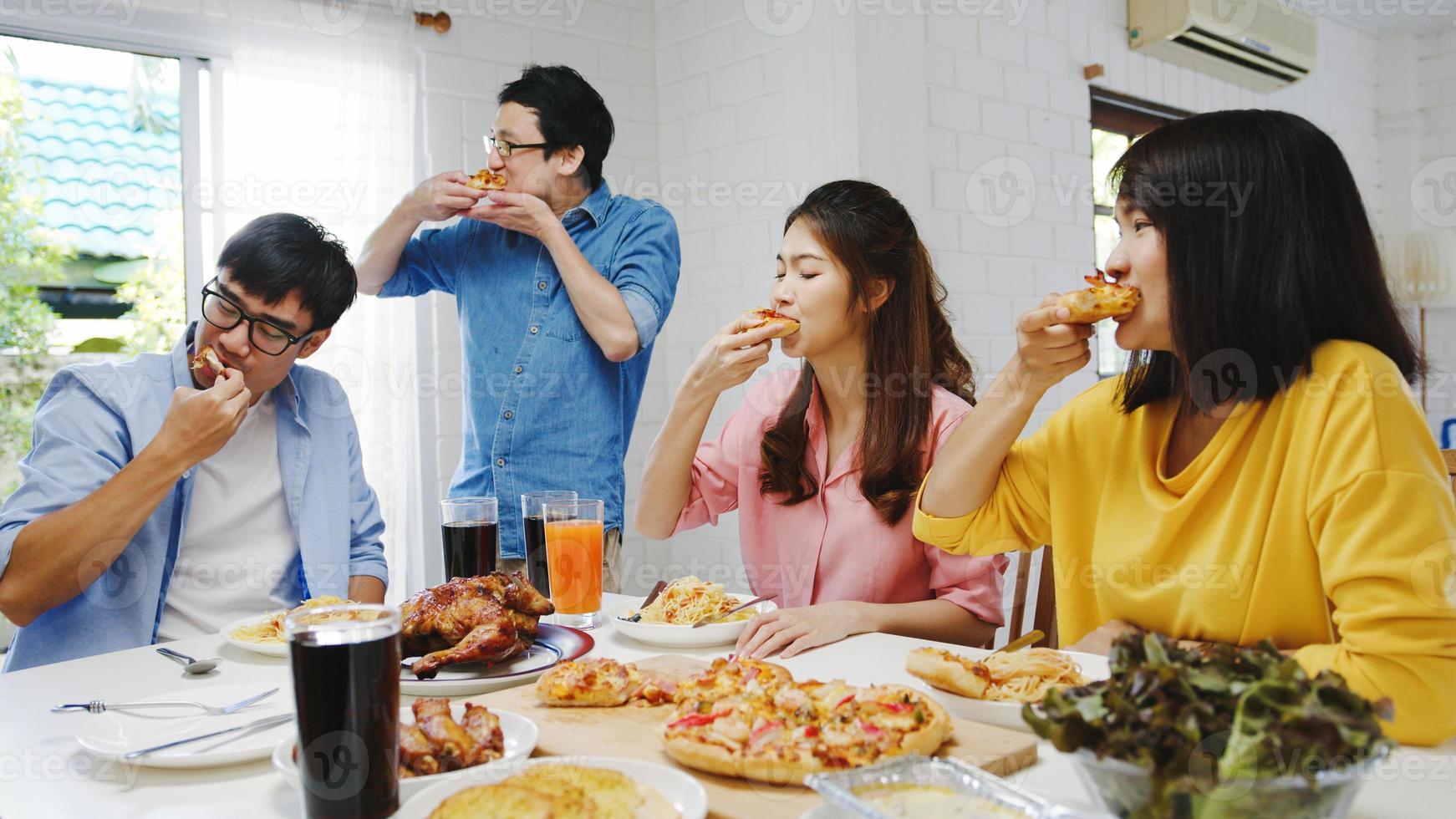 glückliche Gruppe junger Freunde, die zu Hause zu Mittag essen. asien-familienfeier, die pizza essen isst und lacht, mahlzeit genießt, während sie zusammen am esstisch im haus sitzt. feier urlaub und zusammengehörigkeit. foto