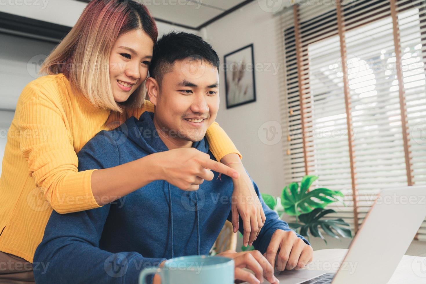 junge asiatische paare, die finanzen verwalten und ihre bankkonten mit laptop-computer und rechner im modernen haus überprüfen. frau und mann erledigen zusammen papierkram und zahlen online steuern auf notebook-pc. foto