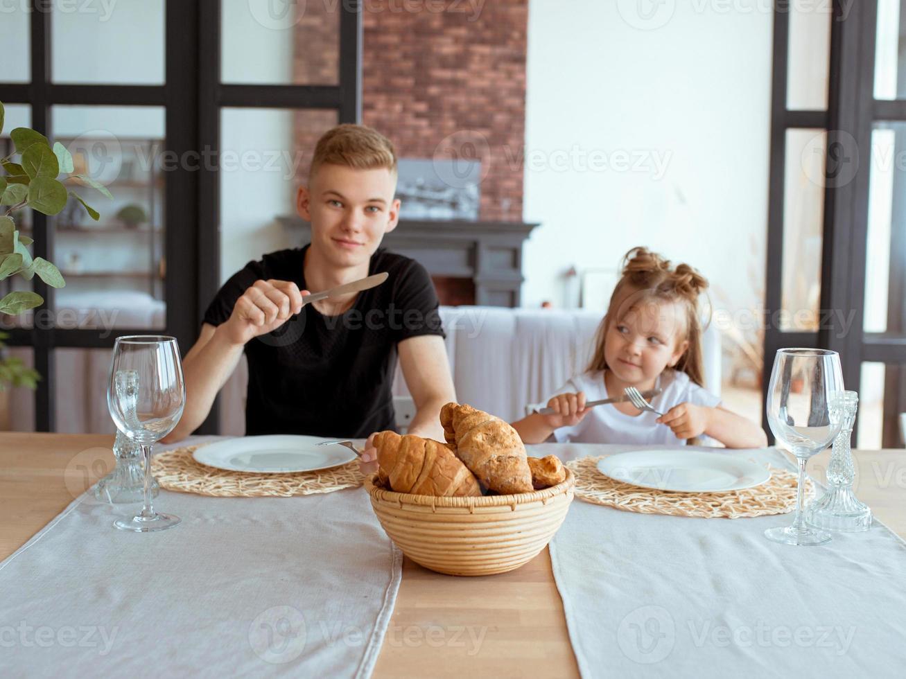 Kaukasische lustige süße Geschwister - kleines Mädchen mit älterem Bruder im Speisesaal im modernen Loft-Interieur. familien-, lebensstil- und esskonzept foto