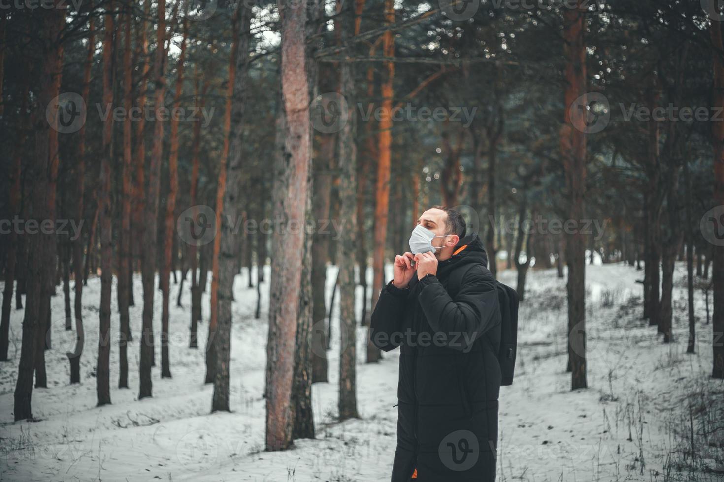 junger Mann mit kurzen Haaren in einer medizinischen Maske im Winterwald. foto