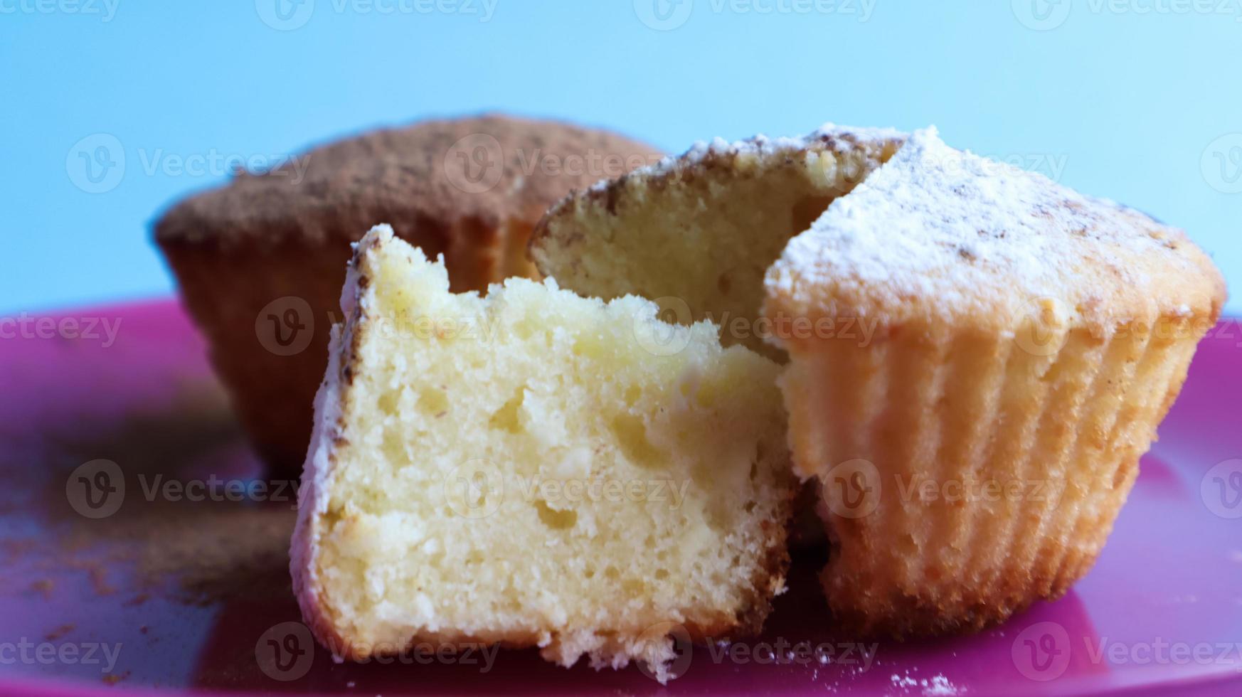 Zwei mit Schokolade und Puderzucker bestreute Quarkkuchen auf einem rosa Teller auf blauem Hintergrund. Nachtisch, ein kleiner Cupcake. Weiß gebackene Kekse mit einer luftigen Textur. Food-Konzept foto