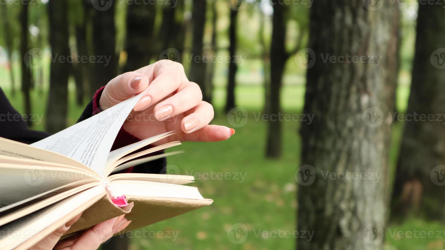 Mädchen, das ein Buch im Park liest. weibliche hände, die seiten des papierbuches draußen umblättern. Der Student bereitet sich auf die Prüfung vor. Literarische Freizeit in der Natur. nahaufnahme, kopierraum. foto