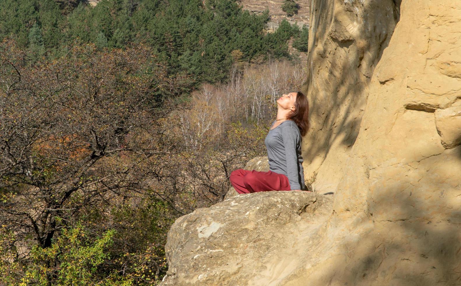 Frau mit geschlossenen Augen und erhobenem Kopf, die an einem Herbsttag in Meditation auf einem Berg im Lotussitz sitzt foto