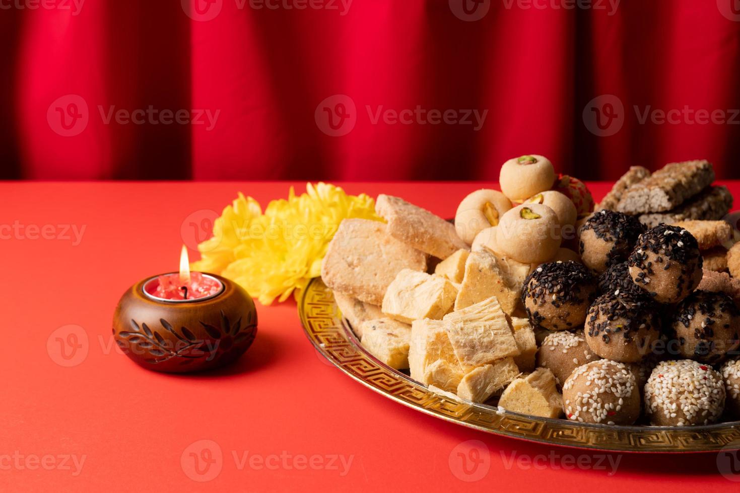 traditionelle indische süßigkeiten auf rotem hintergrund mit kerzen und blumen flach gelegt foto