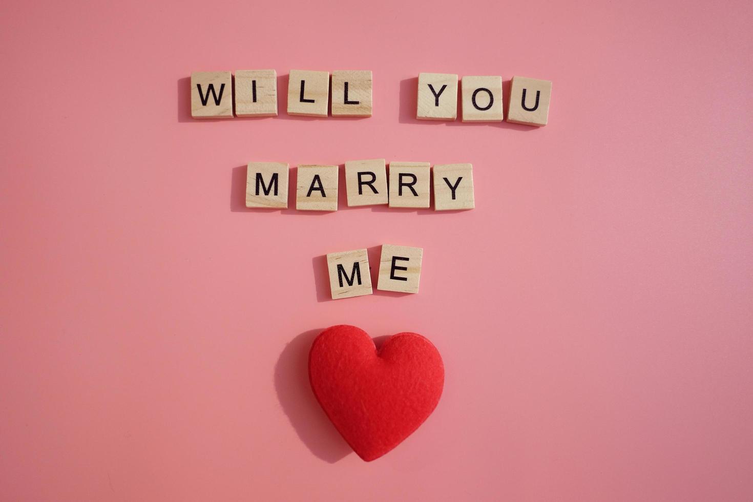 Ein paar rote Herz- und Buchstabenwörter wirst du mich heiraten, isoliert auf rosa Hintergrund. Valentinstag, Geschenk, Nachricht für Liebhaber, Grußkarte. Liebeskonzept. foto