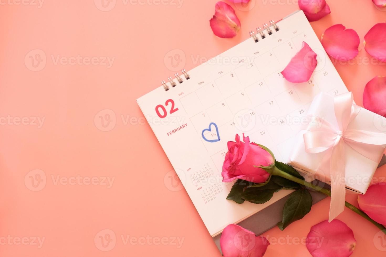 Rosa Rose und eine Geschenkbox im Kalender mit Rosenblättern isoliert auf rosa Hintergrund mit Copyspace für Text. Valentinstag-Konzept. planung terminplaner, veranstaltung, organisator valentinstag. foto