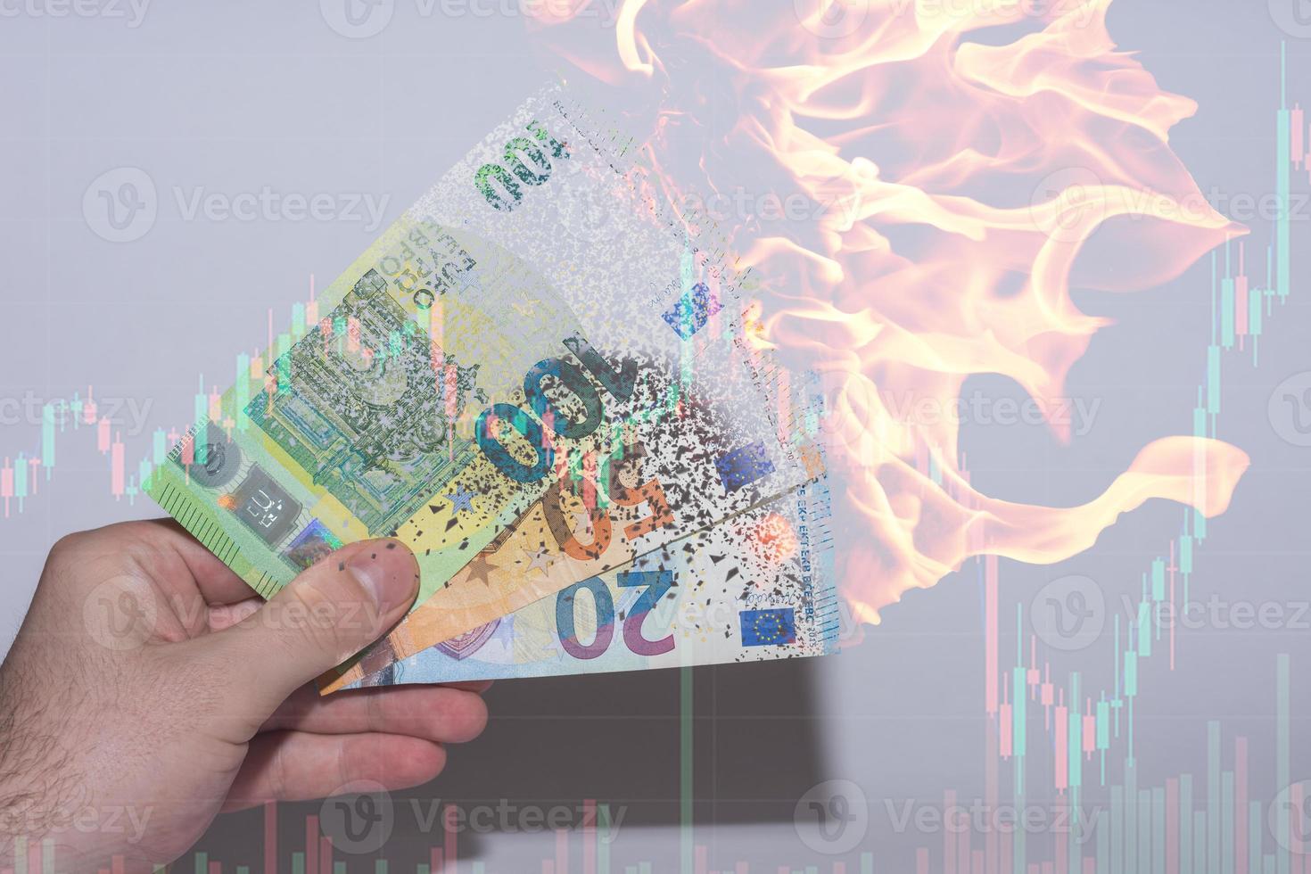 Hand, die drei brennende und sich auflösende Euro-Banknoten mit einem Diagramm aus dem Finanzwesen hält foto
