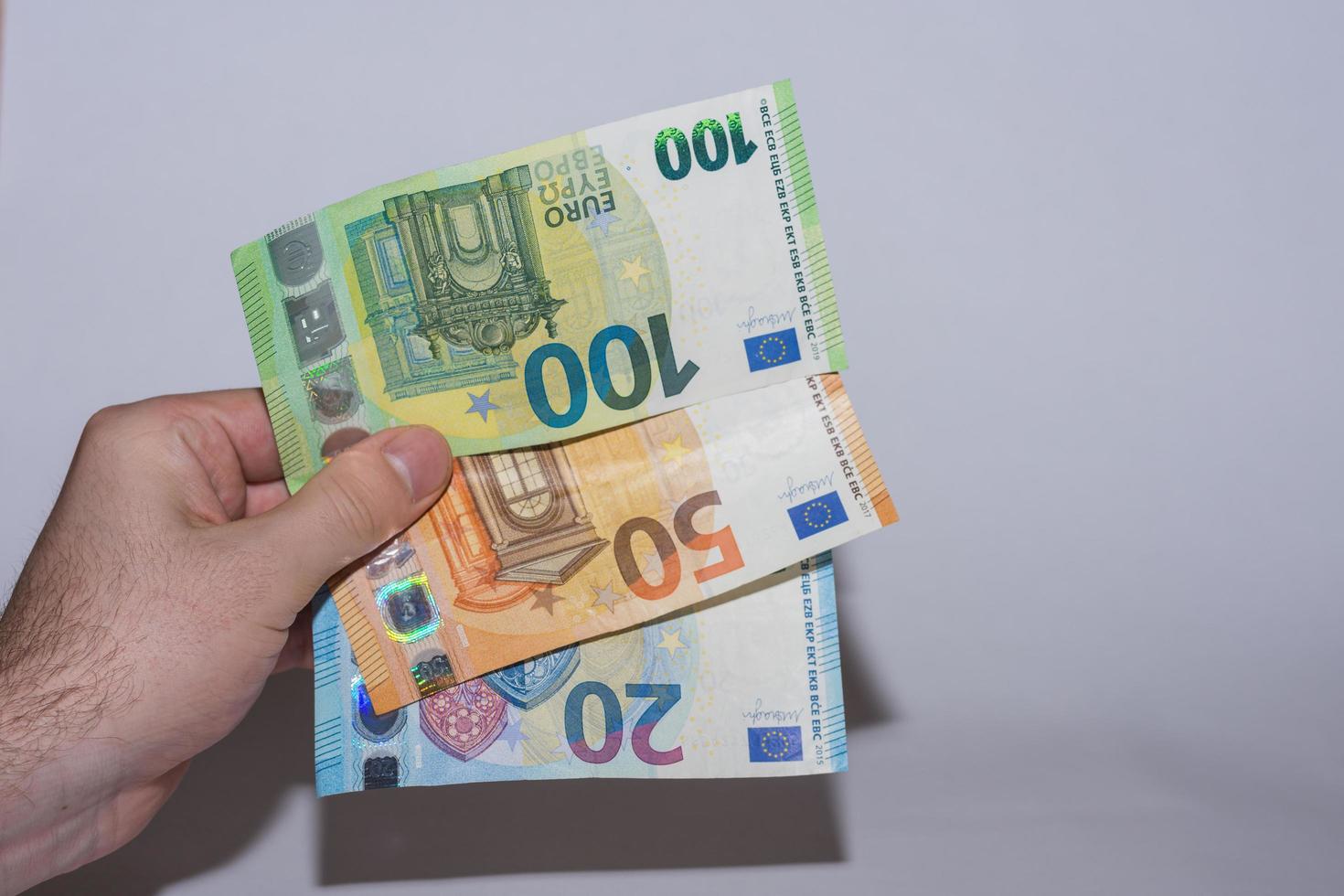 drei Euro-Banknoten, die in einer Hand zur Seite mit Grau gehalten werden foto