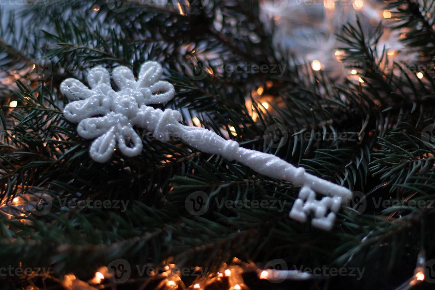 weihnachtsspielzeug, ein weißer schlüssel mit silbernen funkeln auf einem weihnachtsbaumzweig. Bokeh-Hintergrund-Nahaufnahme foto