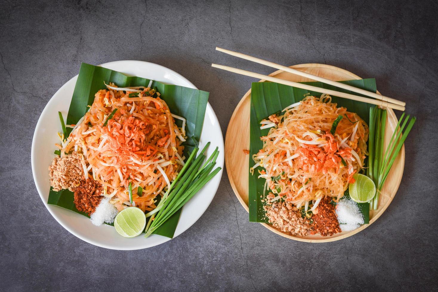 pfannennudelpad thai auf teller serviert auf dem esstisch essen, thailändisches essen gebratene nudeln im thailändischen stil mit garnelen bohnensprossen und garnierung erdnüsse chili puderzucker zitrone limette - draufsicht foto