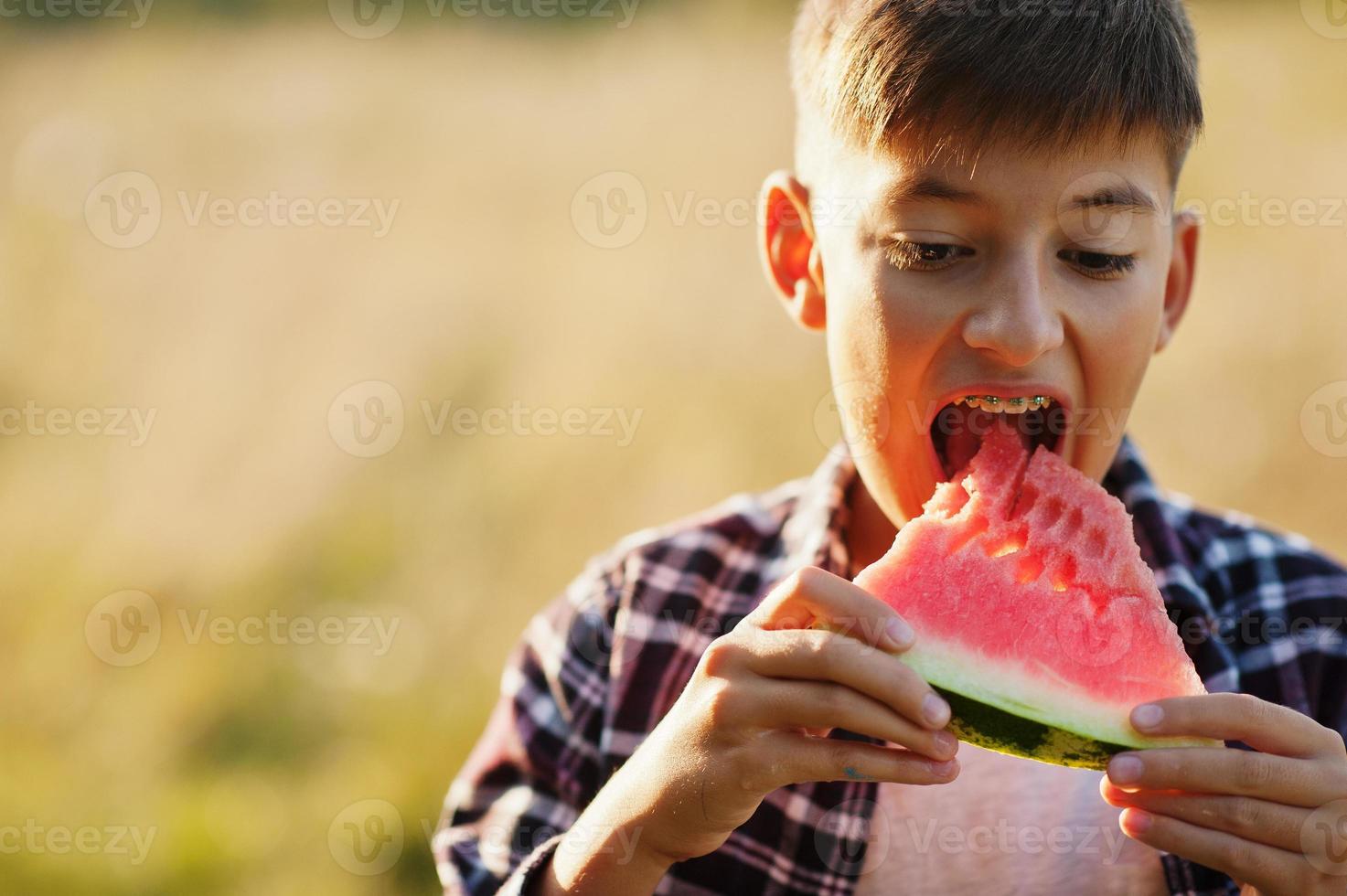 Teenager tragen kariertes Hemd mit Zahnspangen, essen Wassermelone. foto