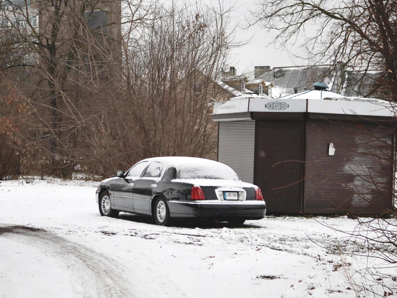 Schwarzes langes Auto, das in der Nähe eines geschlossenen Kiosks steht, der mit weißem Schnee bedeckt ist foto