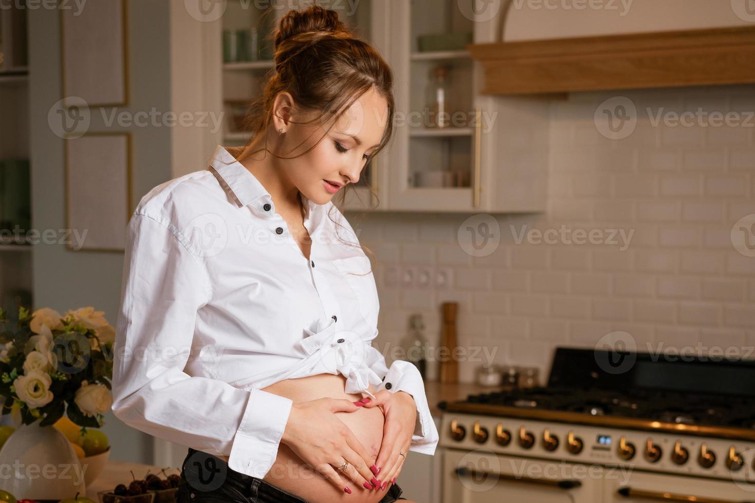 Glückliche schwangere Frau, die am Tisch in der Küche sitzt foto