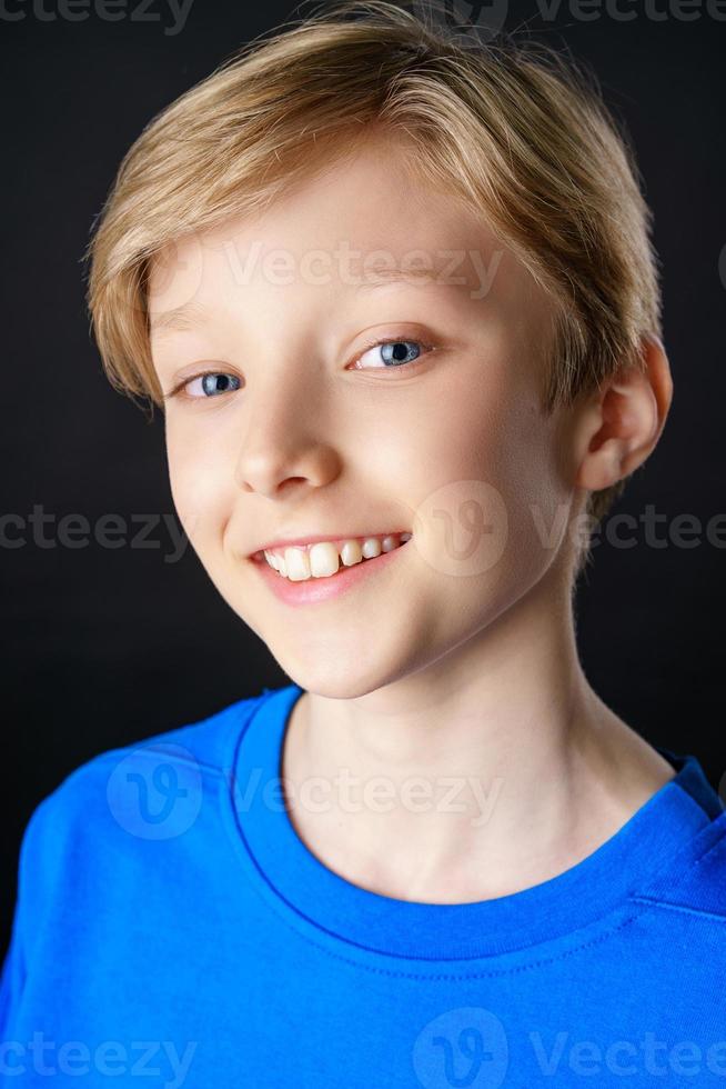 Nahaufnahmeporträt eines Jungen in einem blauen T-Shirt auf einem schwarzen Hintergrund, der lächelt, foto