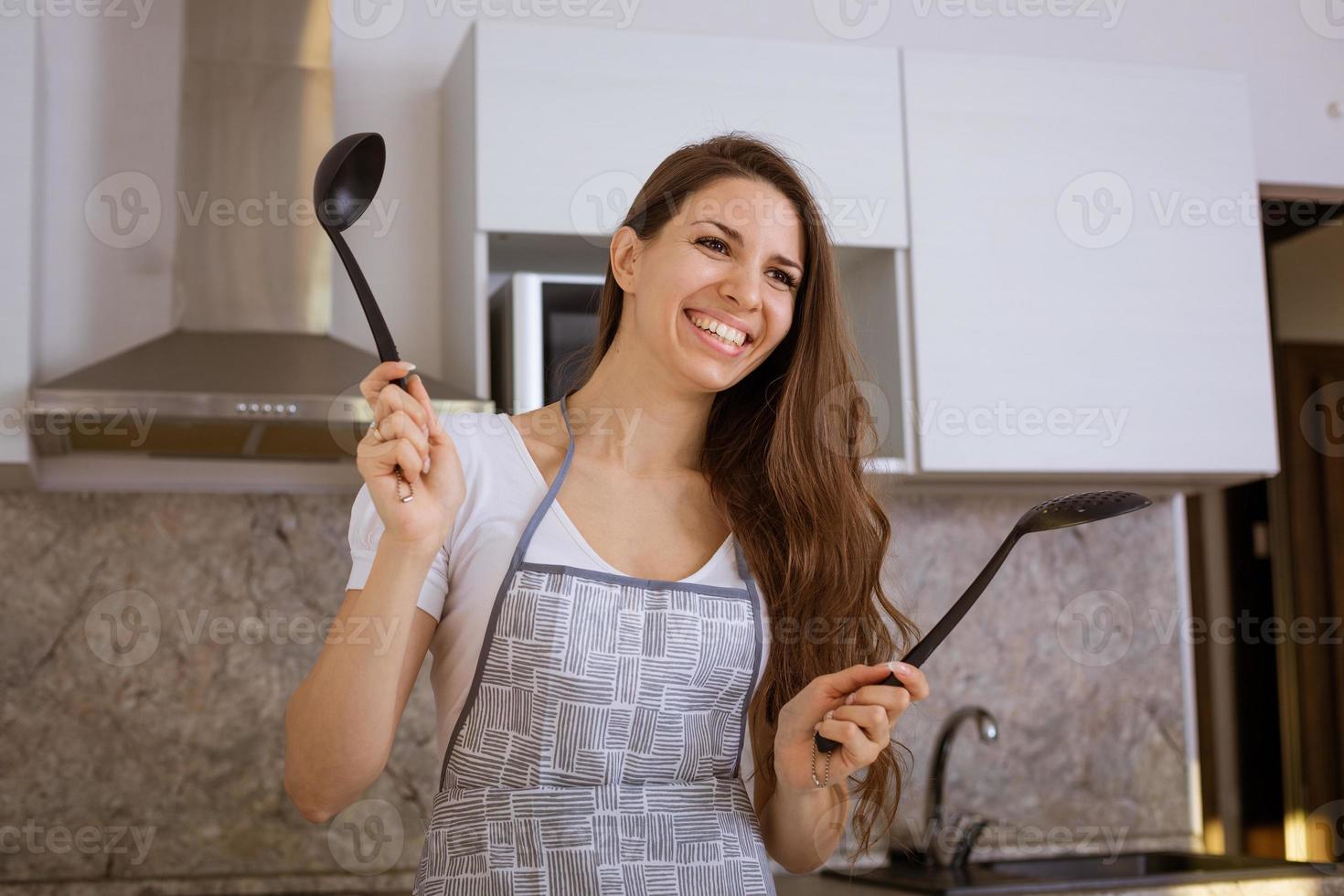 junge Frau in der Küche mit Schöpfkelle in der Hand lächelnd foto
