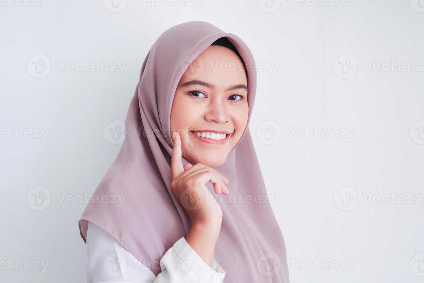 junge asiatische islamfrau mit kopftuch mit sauberer, frischer weißer haut, die das gesicht mit den fingern sanft in schönheitspose berührt. indonesische Frau. Beauty-Konzept isoliert auf grauem Hintergrund foto