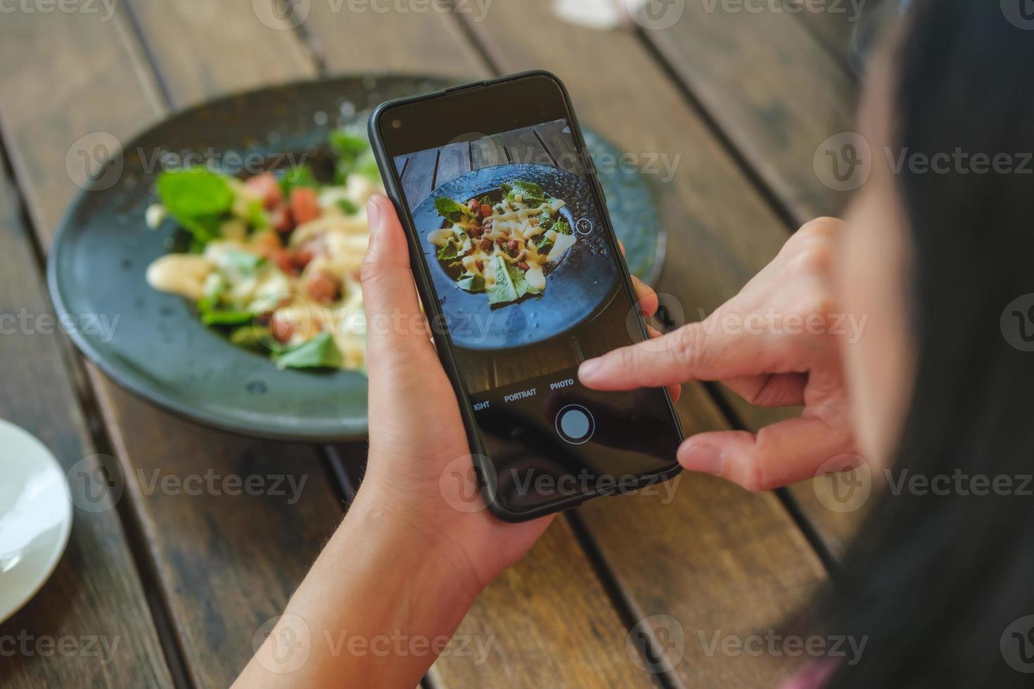 Frau benutzt Handy, macht ein Foto von Salat, bevor sie im Restaurant isst