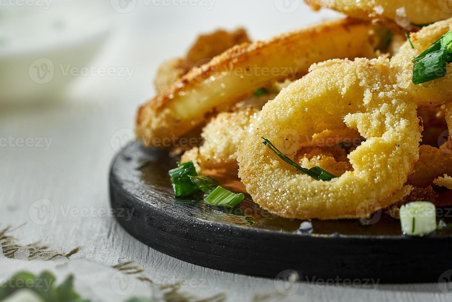 Zwiebelringe im Teig, bestreut mit Gemüse auf weißem Hintergrund in einer Unschärfe. ungesundes aber leckeres essen. foto