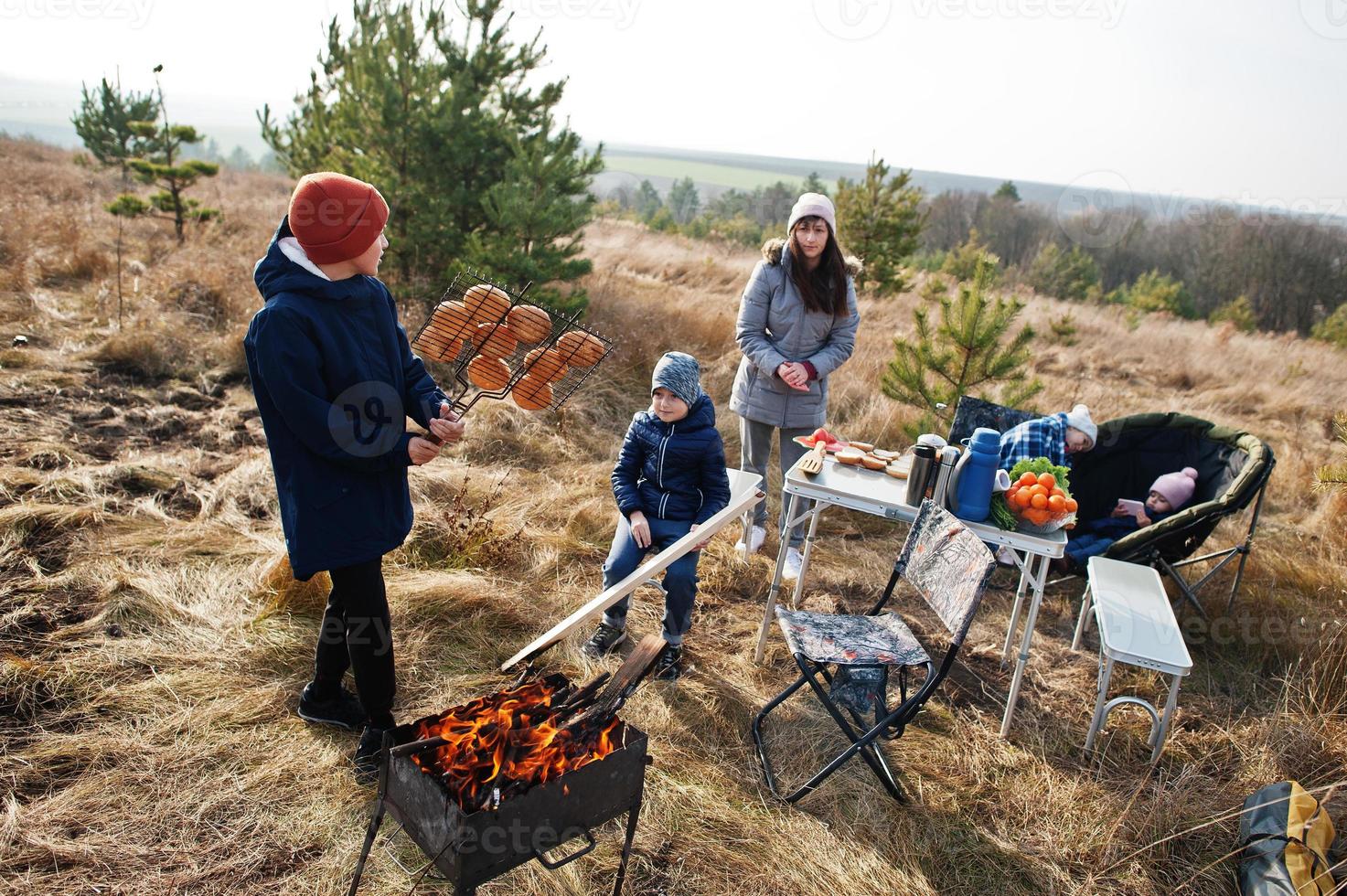 Familie beim Grillen auf einer Terrasse im Pinienwald. Grilltag mit Grill. foto